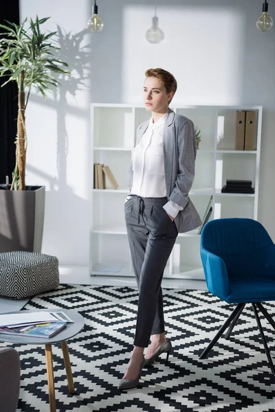 Mulher de negócios jovem na moda em pé no escritório moderno e olhando para longe — Fotografia de Stock
