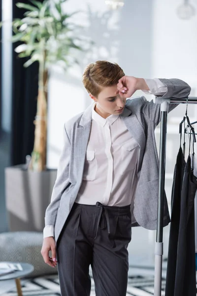 Beautiful young fashion designer leaning on bar with dresses — Stock Photo