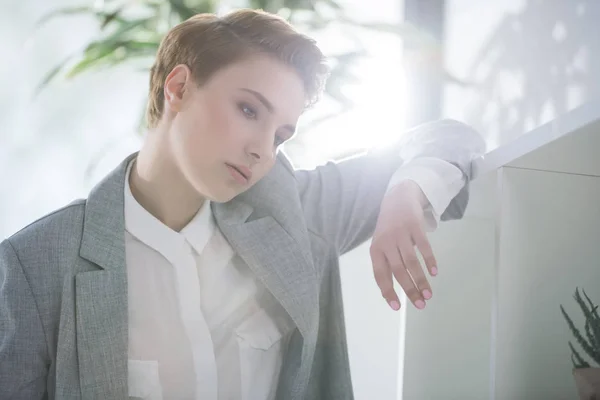Pensativa joven mujer de negocios apoyada en bokshelves en la oficina — Stock Photo