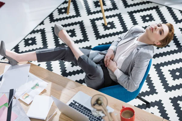 Vista de ángulo alto de atractiva joven mujer de negocios relajarse en la silla en la oficina - foto de stock