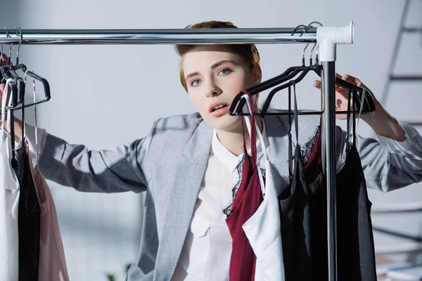 Femme élégante debout entre les vêtements suspendus sur rack — Photo de stock