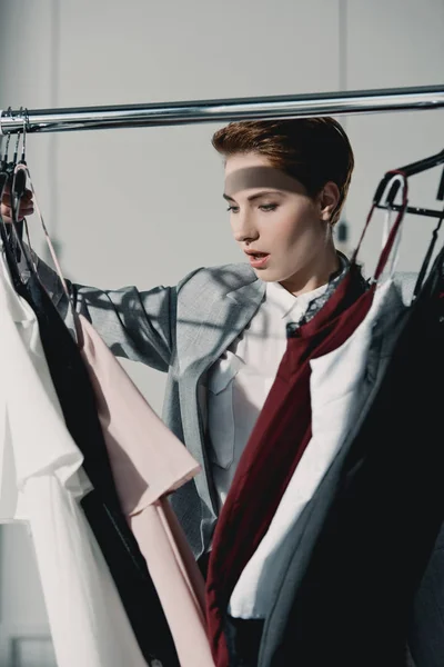 Mujer joven emocionada eligiendo ropa en la tienda - foto de stock