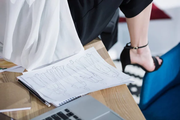 Cropped shot of fashion designer sitting on work table with sketches — Stock Photo