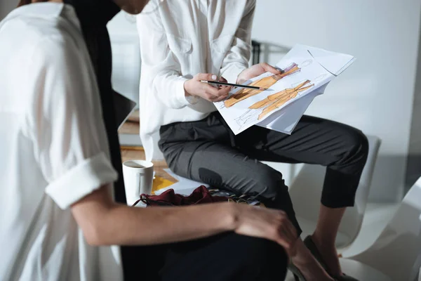 Croped shot of fashion designers sitting on table and discovering sketches — Stock Photo