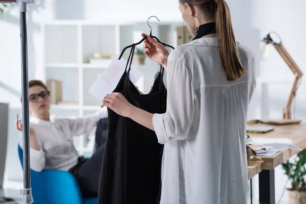 Jóvenes diseñadores de moda discutiendo nuevo vestido en percha — Stock Photo