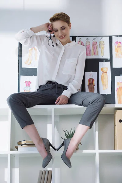 Beautiful stylish fashion designer sitting on bookshelves — Stock Photo