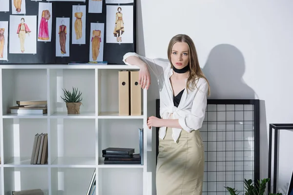 Elegante diseñador de moda apoyado en estanterías en la oficina - foto de stock