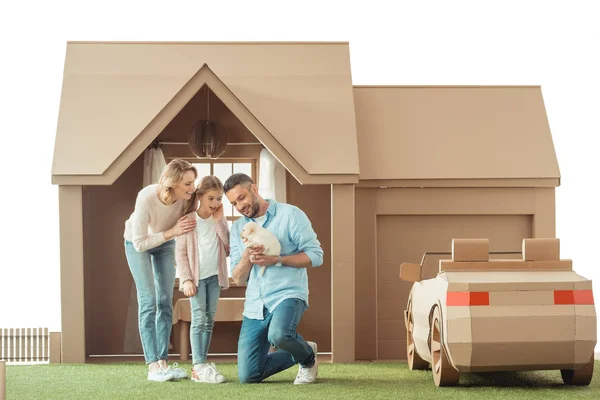 Bella famiglia con adorabile cucciolo labrador di fronte alla casa di cartone isolato su bianco — Foto stock