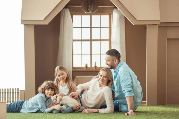 Glückliche junge Familie liegt mit ihrem Welpen auf dem Hof eines Papphauses — Stockfoto