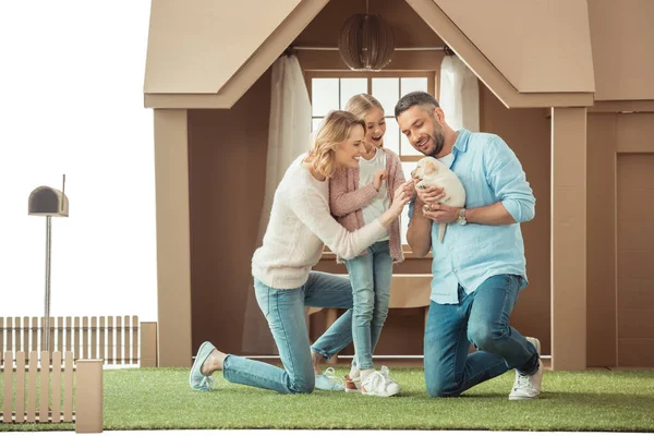 Счастливая семья с восхитительным щенком лабрадора перед картонным домиком — стоковое фото