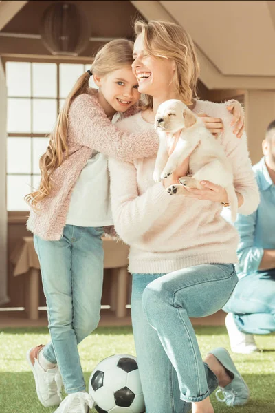 Улыбающиеся мать и дочь играют с очаровательным щенком лабрадора — стоковое фото
