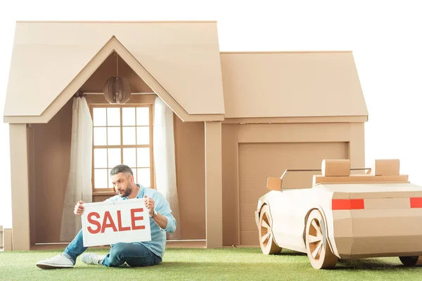 Homme tenant enseigne de vente en face de la maison en carton isolé sur blanc — Photo de stock