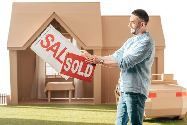 Homme tenant vente et vendu des panneaux en face de la maison en carton isolé sur blanc — Photo de stock