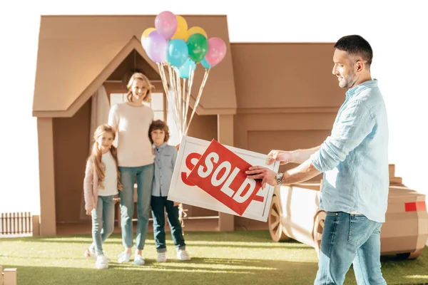 Счастливая молодая семья переезжает в новый кардбордовый дом, изолированный на белом — стоковое фото