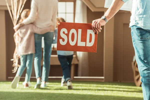 Cropped shot of man holding sold signboard with young family moving into new cardbord house — Stock Photo