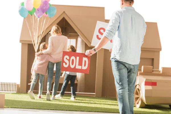 Hombre sosteniendo letrero vendido con la familia joven que se mueve en nueva casa de cardbord aislado en blanco - foto de stock