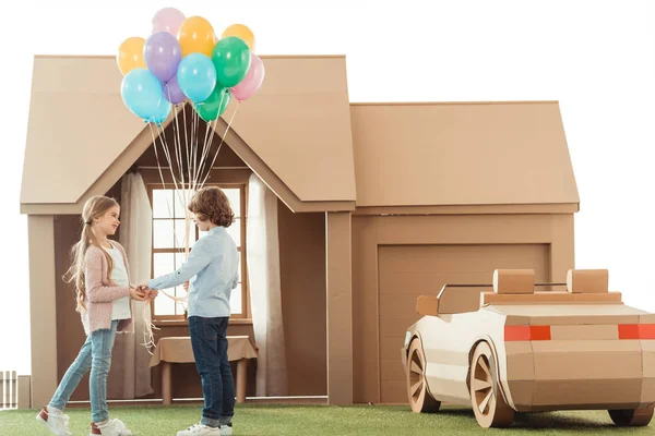 Petit enfant présentant des ballons à petite amie devant la maison en carton isolé sur blanc — Photo de stock