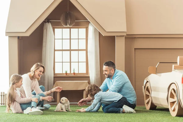 Bela família com cachorrinho adorável no quintal da casa de papelão — Fotografia de Stock