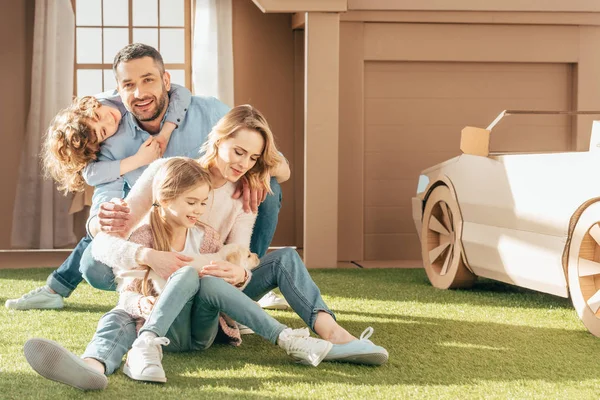 Young family with little labrador puppy on yard of cardboard house — Stock Photo