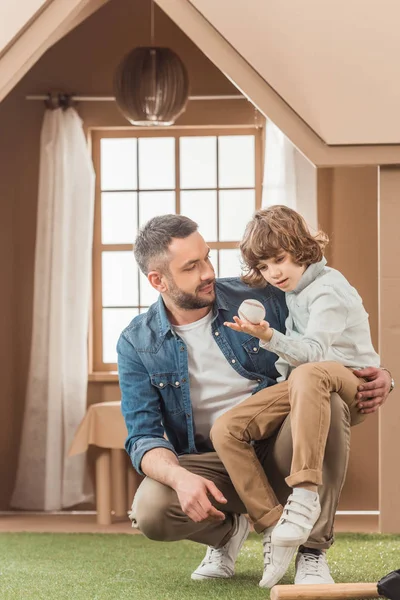 Happy father teaching his son how to play baseball in front of cardboard house — Stock Photo