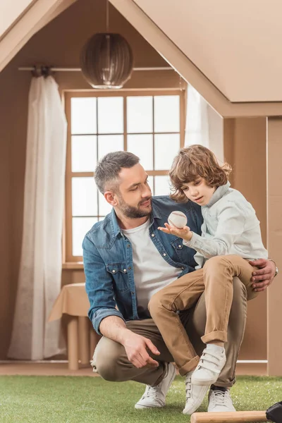 Feliz padre enseñando a su hijo a jugar béisbol en frente de la casa de cartón - foto de stock