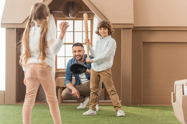 Père enseignant à ses enfants comment jouer au baseball devant une maison en carton — Photo de stock