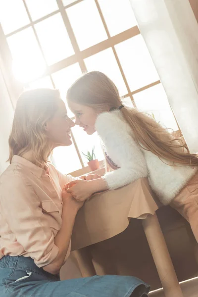 Hermosa madre e hija abrazándose delante de la ventana de luz - foto de stock