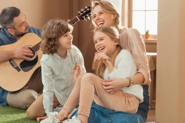 Man playing guitar for his happy family at new cardboard house — Stock Photo