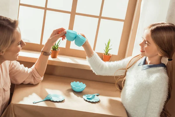 Mother and daughter having tea party in cardboard house and clinking cups — Stock Photo