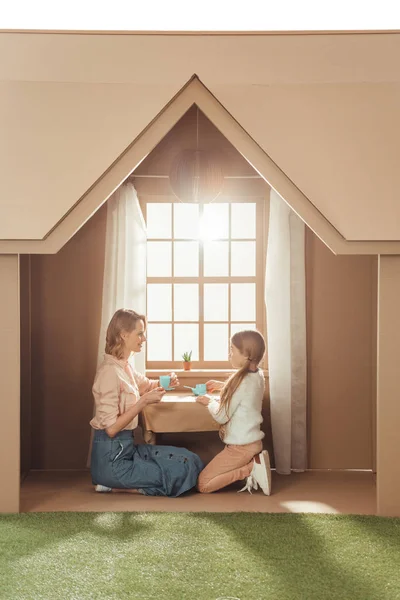 Beautiful mother and daughter having tea party in cardboard house — Stock Photo