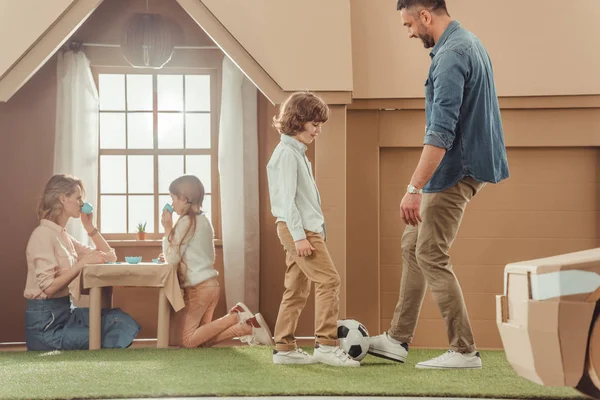 Feliz padre enseñando su som a jugar al fútbol en el patio de la casa de cartón - foto de stock