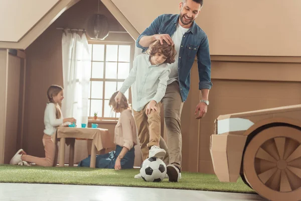 Bonito pai ensinando seu som para jogar futebol no quintal da casa de papelão — Fotografia de Stock