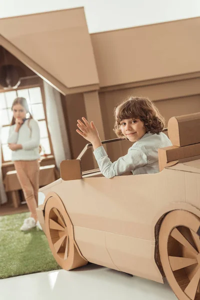 Щаслива маленька дитина приїхала за дівчиною на картонній машині — стокове фото