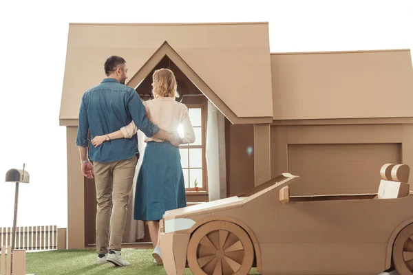 Rear view of couple embracing in front of cardboard house isolated on white — Stock Photo