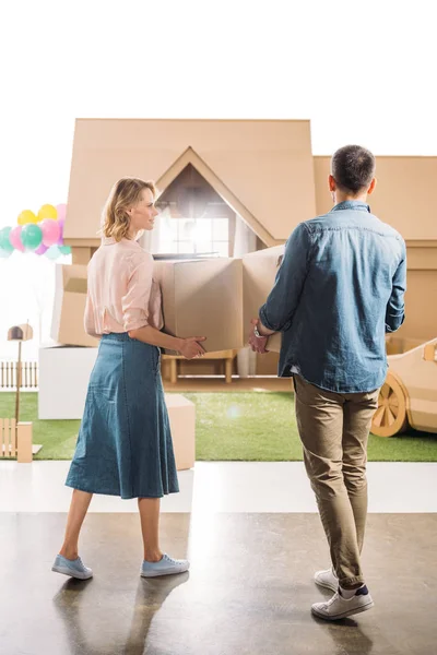 Vista trasera de la pareja que se mueve en la nueva casa de cartón aislado en blanco - foto de stock