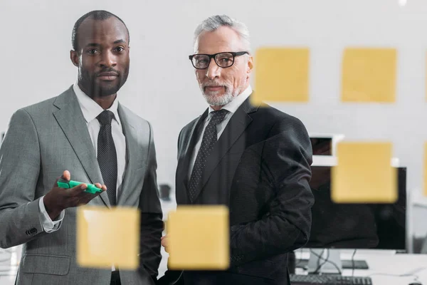 Foco seletivo de empresários multiculturais olhando para notas durante reunião no escritório — Fotografia de Stock
