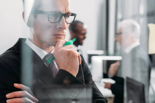 Messa a fuoco selettiva dell'uomo d'affari concentrato che osserva le note appiccicose mentre i colleghi multiculturali che discutono nell'ufficio — Foto stock