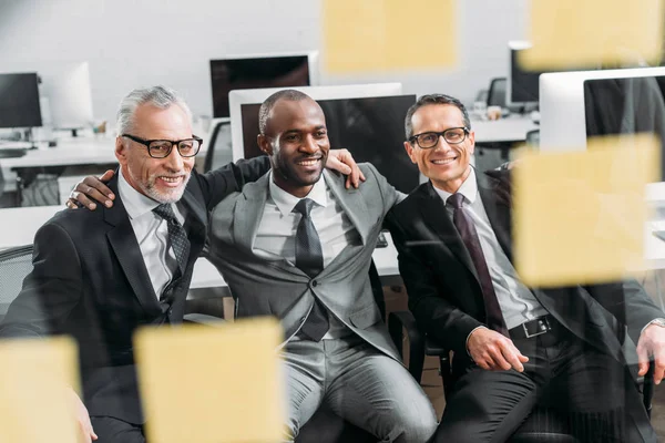 Hombres de negocios sonrientes multiculturales mirando notas durante la reunión en la oficina - foto de stock