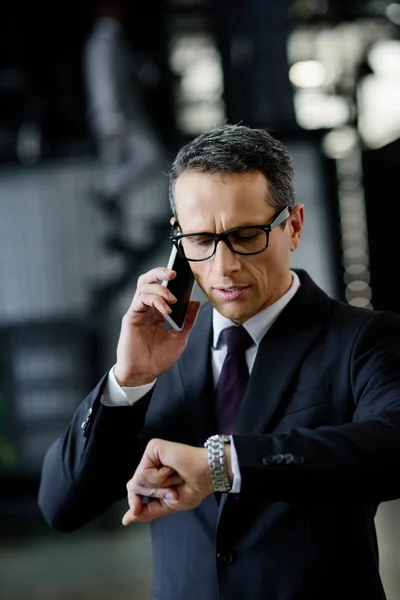 Retrato del hombre de negocios comprobando el tiempo mientras habla en el teléfono inteligente - foto de stock