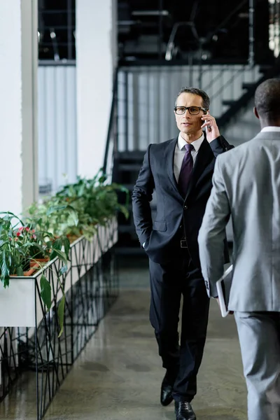 Confident businessman talking on smartphone while walking in office — Stock Photo