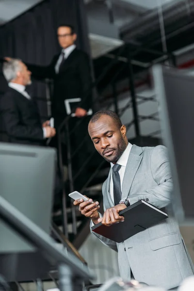 Selective focus of african american businessman with smartphone checking time — Stock Photo
