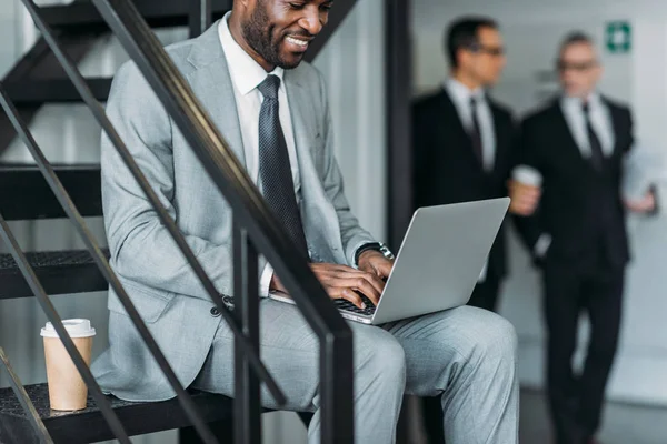 Vista parcial de sonriente hombre de negocios afroamericano trabajando en el ordenador portátil - foto de stock