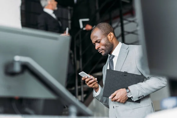 Selektiver Fokus eines afrikanisch-amerikanischen Geschäftsmannes mit Dokumenten per Smartphone — Stockfoto