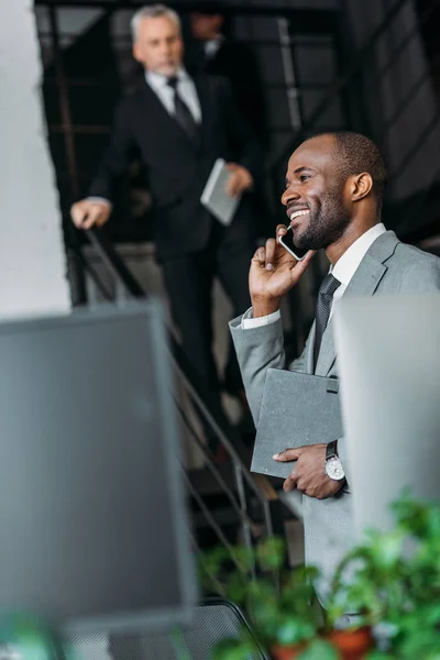 Selektiver Fokus eines lächelnden afrikanisch-amerikanischen Geschäftsmannes, der auf dem Smartphone spricht — Stockfoto