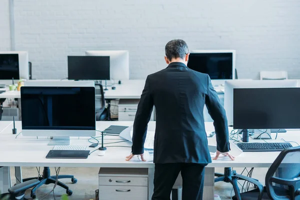 Vue arrière de l'homme d'affaires debout sur le lieu de travail dans le bureau — Photo de stock