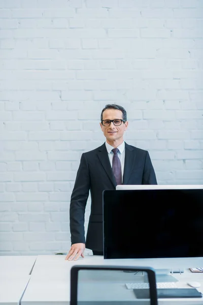 Porträt eines lächelnden Geschäftsmannes, der am Arbeitsplatz im Büro in die Kamera blickt — Stockfoto