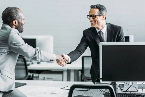 Side view of multiehtnic business colleagues shaking hands in office — Stock Photo
