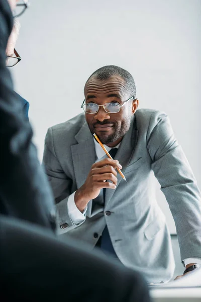 Teilbild eines lächelnden afrikanisch-amerikanischen Geschäftsmannes, der bei einem Treffen im Büro Kollegen ansieht — Stockfoto