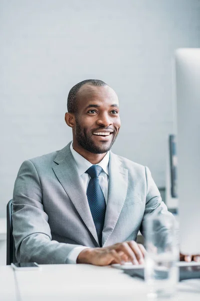 Retrato del hombre de negocios afroamericano sonriente que trabaja en la computadora en el lugar de trabajo - foto de stock