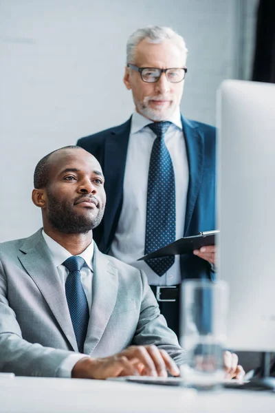 Коллеги по многонациональному бизнесу смотрят на экран компьютера на рабочем месте в офисе — стоковое фото
